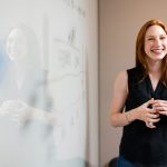 smiling woman presenting at whiteboard