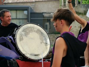 Young person playing a large drum with a man watching
