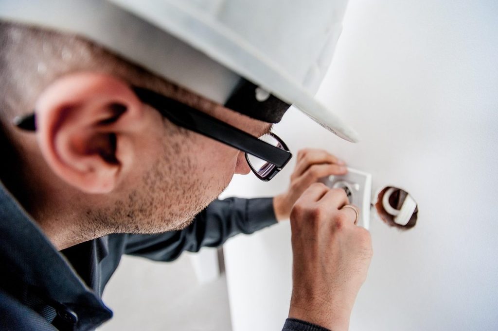 Un homme en casque et lunettes fixe une prise électrique sur un mur