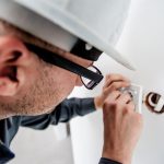 Un homme en casque et lunettes fixe une prise électrique sur un mur