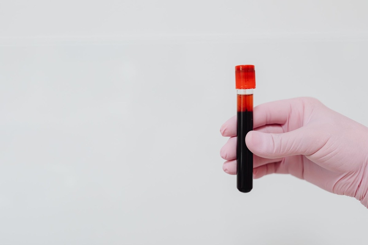 Main gantée tenant un tube à essai avec liquide noir et bouchon rouge sur fond blanc