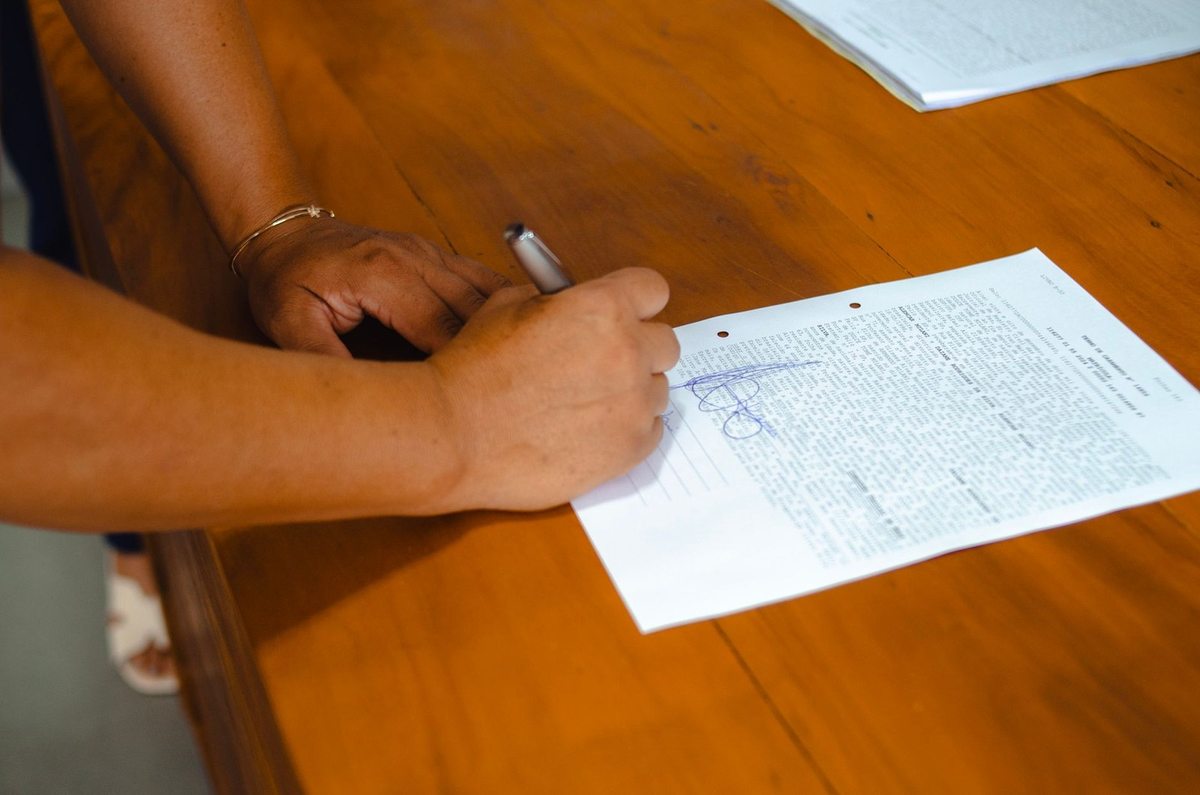 Main droite tenant une plume et écrivant sur un papier posé sur une table en bois