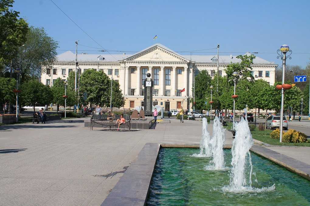Bâtiment avec colonnes et fontaine devant, avenue bordée d'arbres